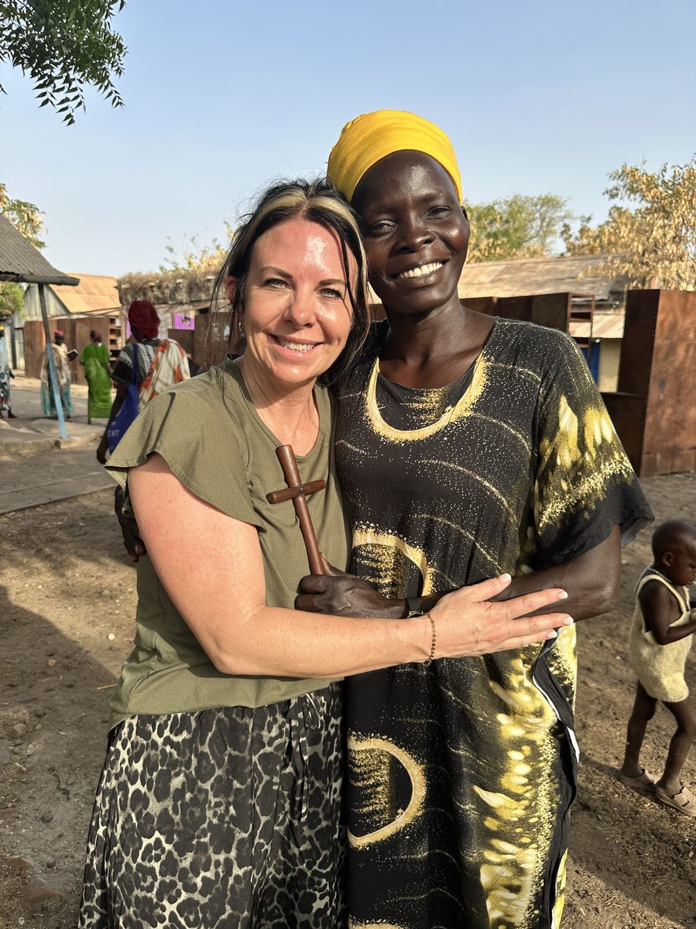 Jodi and a friend holding a wooden cross together in a village center