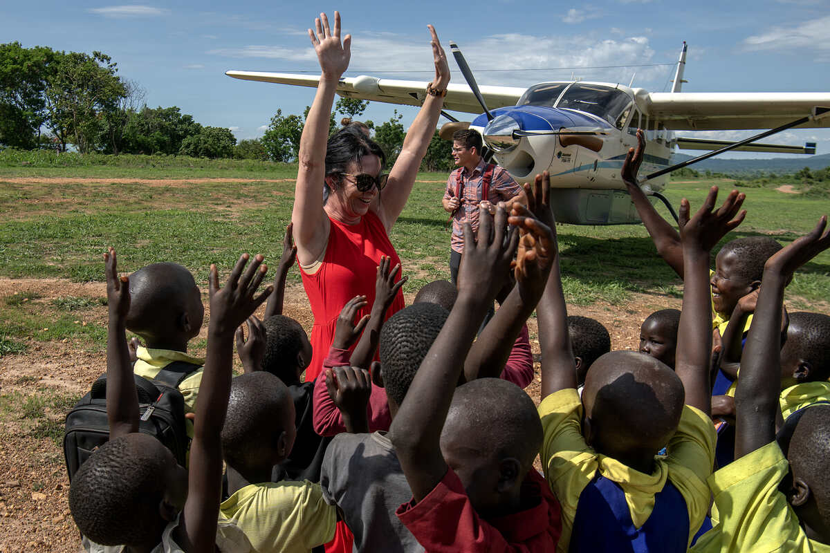 Jodi celebrating with schoolchildren beside a bush plane on a grass airstrip